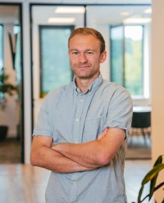 Man in light blue shirt in office smiling at the camera