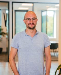 Man in light shirt and glasses in office smiling at the camera