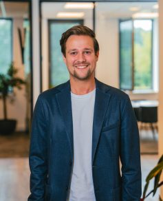 Man in blue jacket in office smiling at the camera
